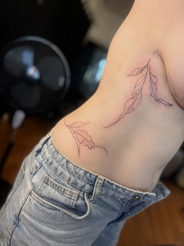 Delicate fine-line leaf tattoo on rib and hip.