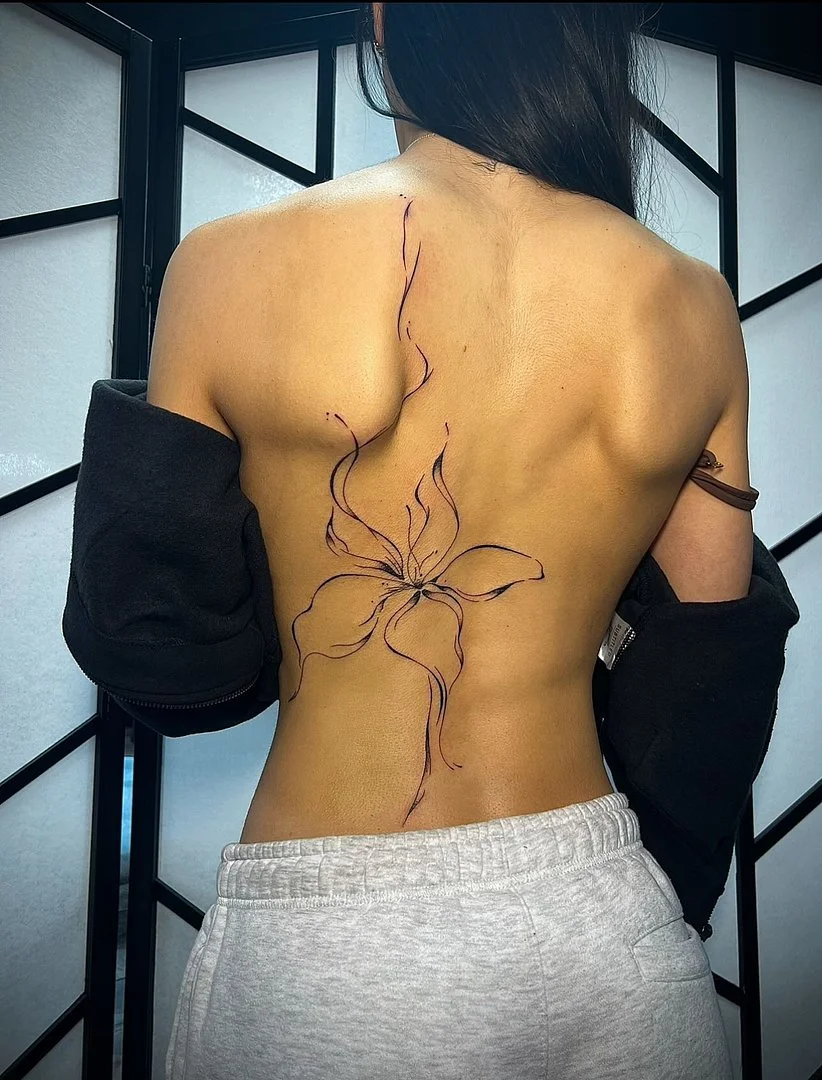 Large fine-line flower tattoo on a woman's back.