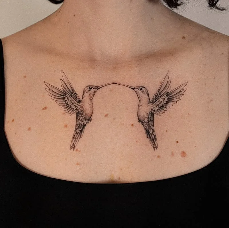 Realistic black and grey tattoo of two hummingbirds on chest.