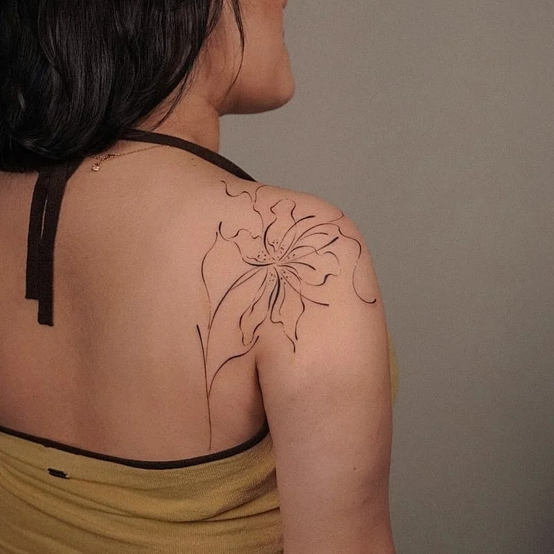 Delicate fine-line flower tattoo on shoulder.