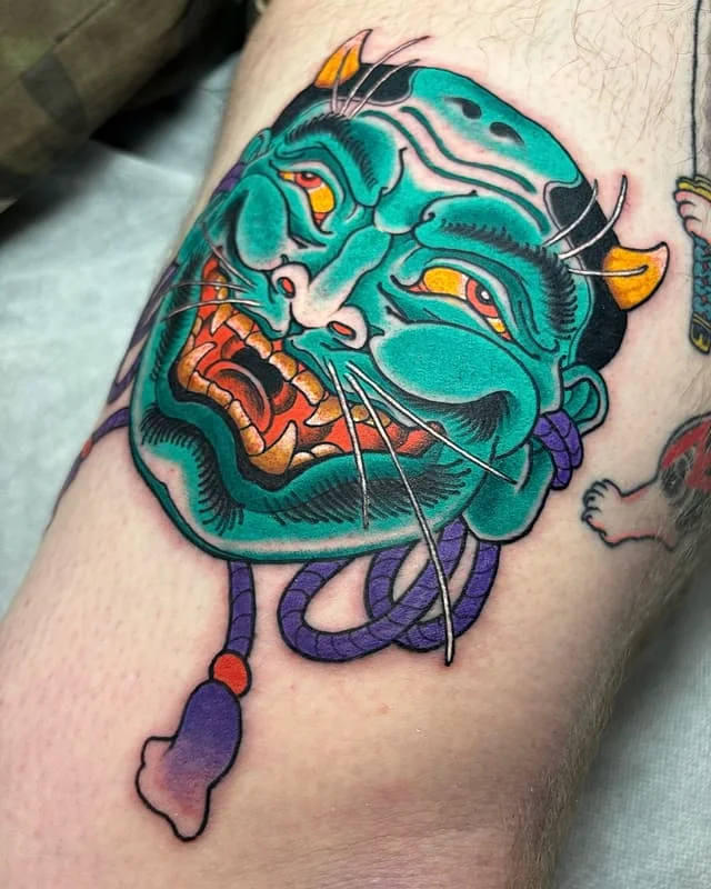 Vibrant illustrative tattoo of a demon face on leg.