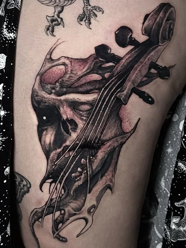 Realistic skull and violin tattoo on thigh.