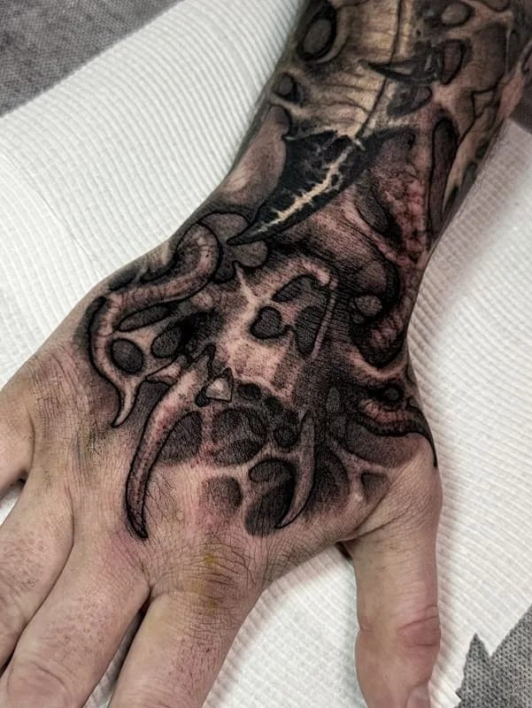 Black-and-grey octopus and skull tattoo on hand.