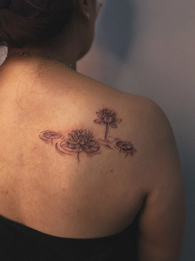 Fine-line lotus flower tattoo on shoulder and back.