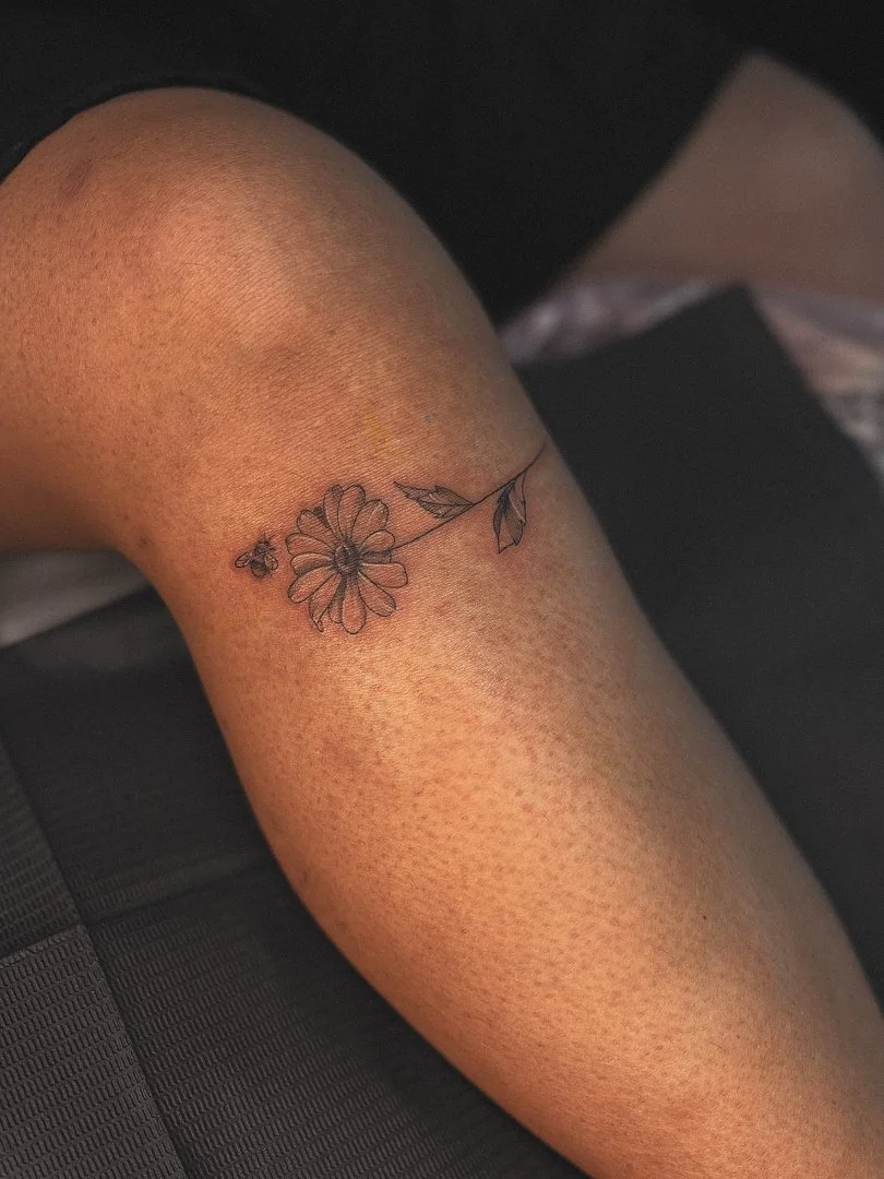 Fine-line flower and bee tattoo on a leg.