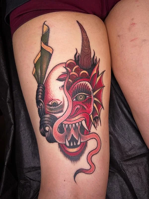 Vibrant traditional demon mask tattoo on thigh.