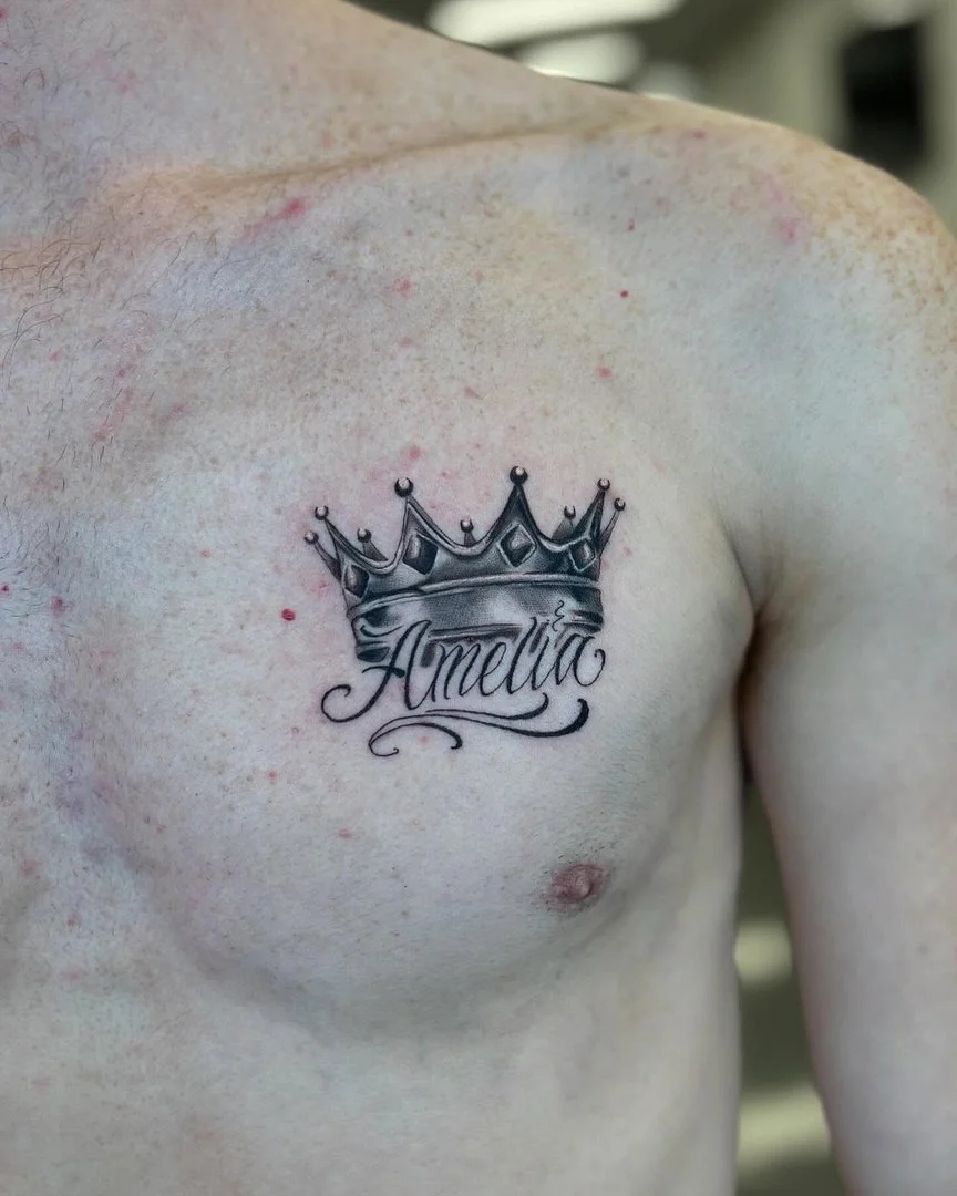 Black-and-grey crown tattoo with the name Amelia on chest.