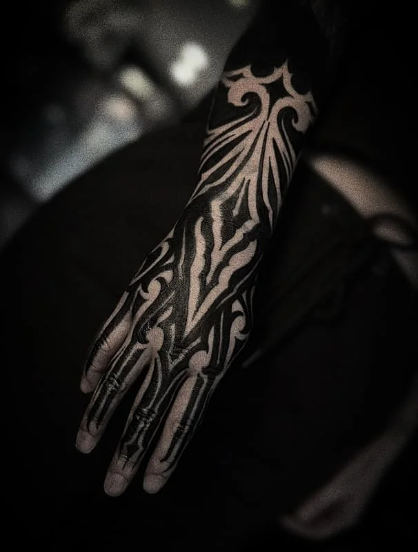 Intricate black tribal tattoo on hand and arm.