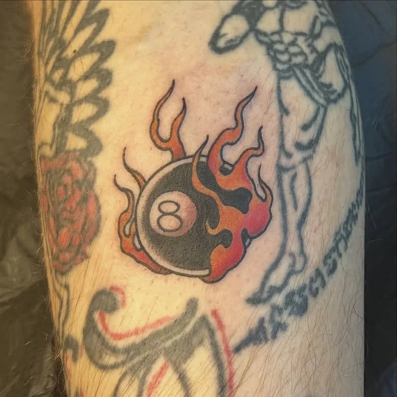 Traditional eight-ball tattoo with flames on arm.