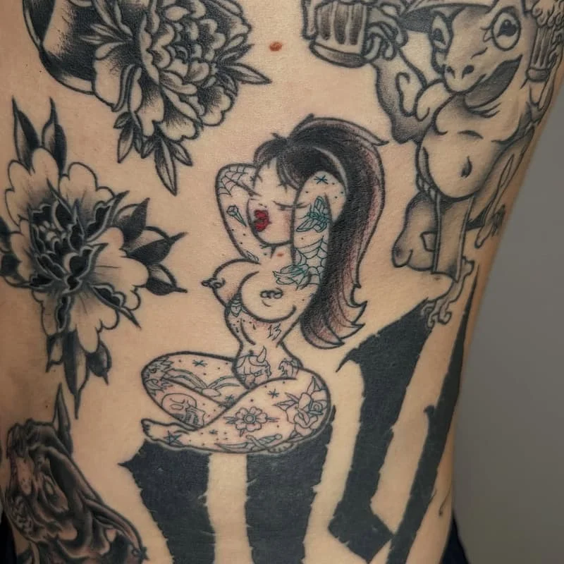 Illustrative tattoo of a pin-up girl with flowers and a frog.