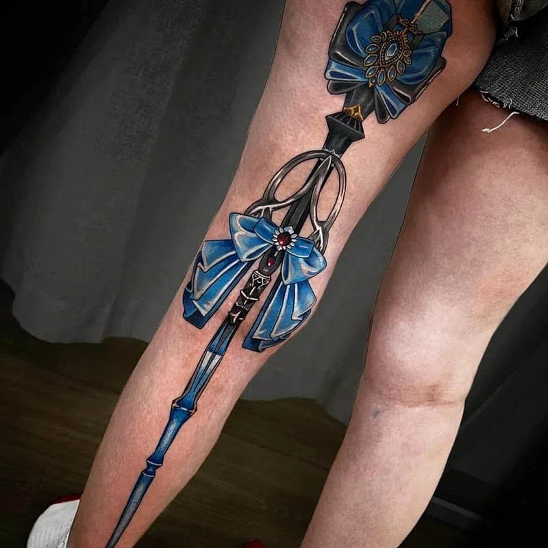 Large illustrative leg tattoo with blue bow and ornate design.