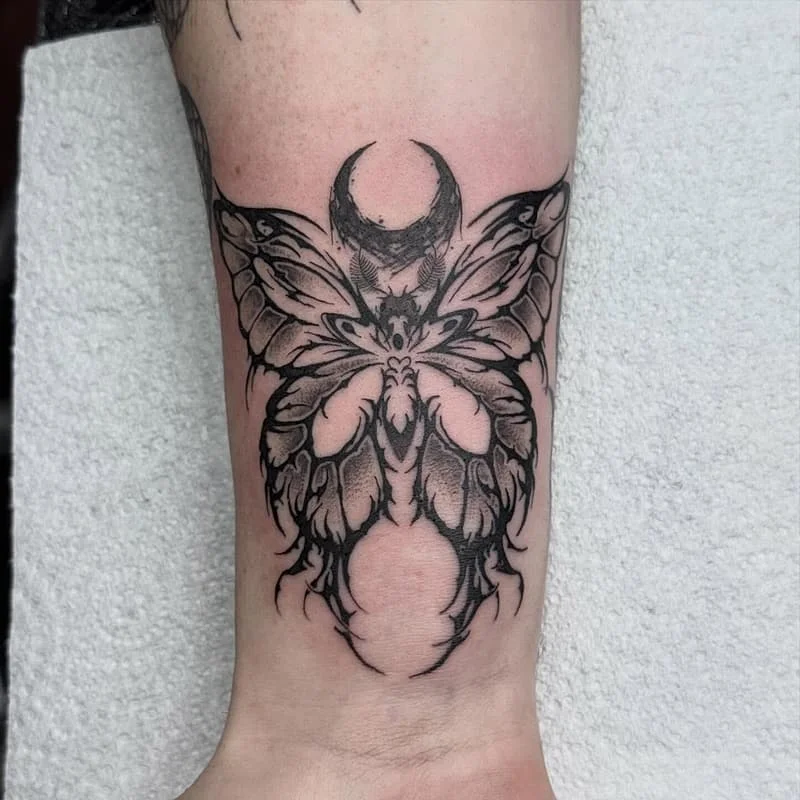 Blackwork butterfly tattoo with crescent moon on forearm.