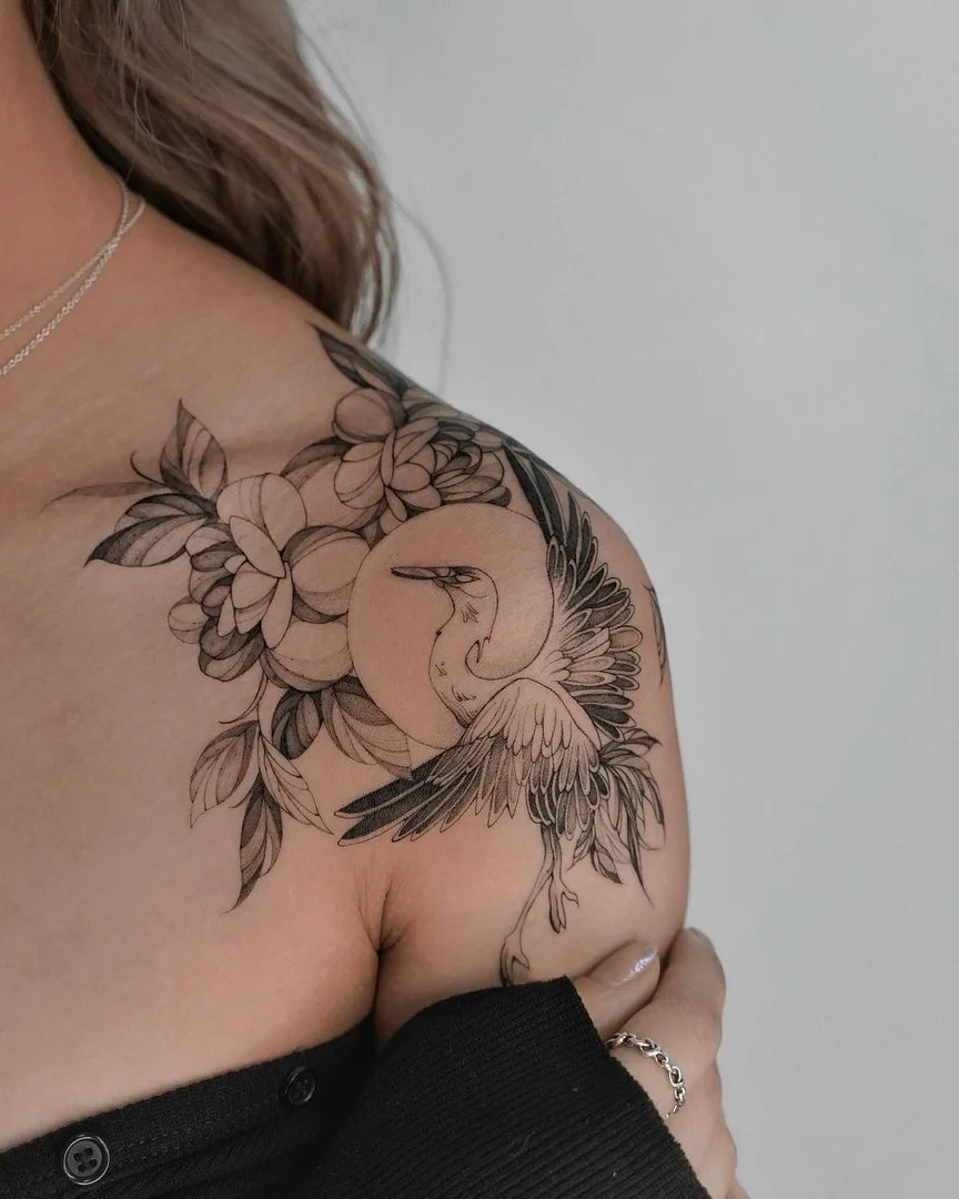 Black-and-grey bird and floral tattoo on shoulder.