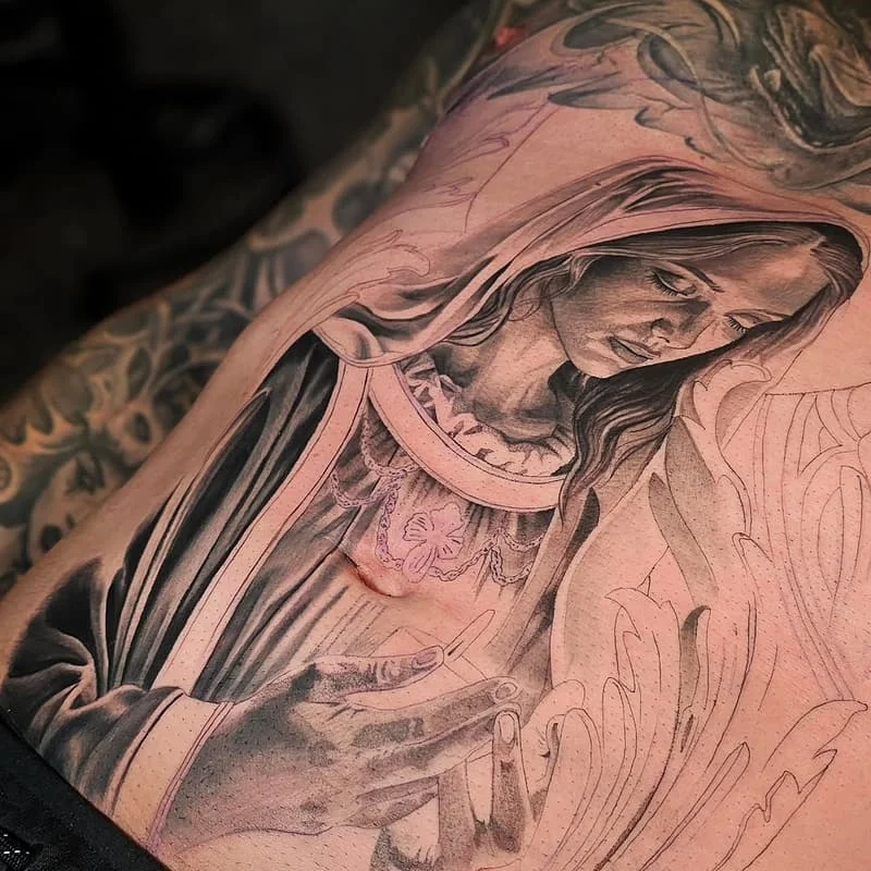 Realistic black-and-grey tattoo of a religious figure on chest.