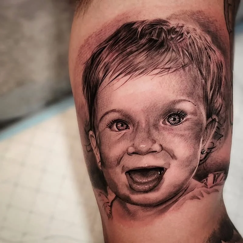 Realistic black-and-grey tattoo of a baby's face on calf.