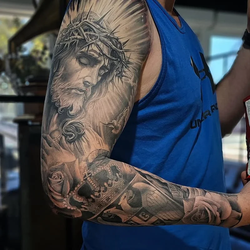 Detailed full-sleeve tattoo of Jesus with roses and skulls.