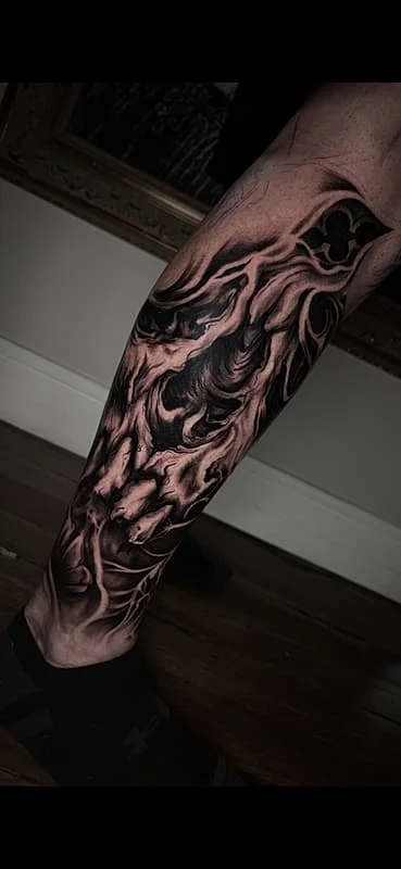 Large black-and-grey abstract tattoo on a calf.