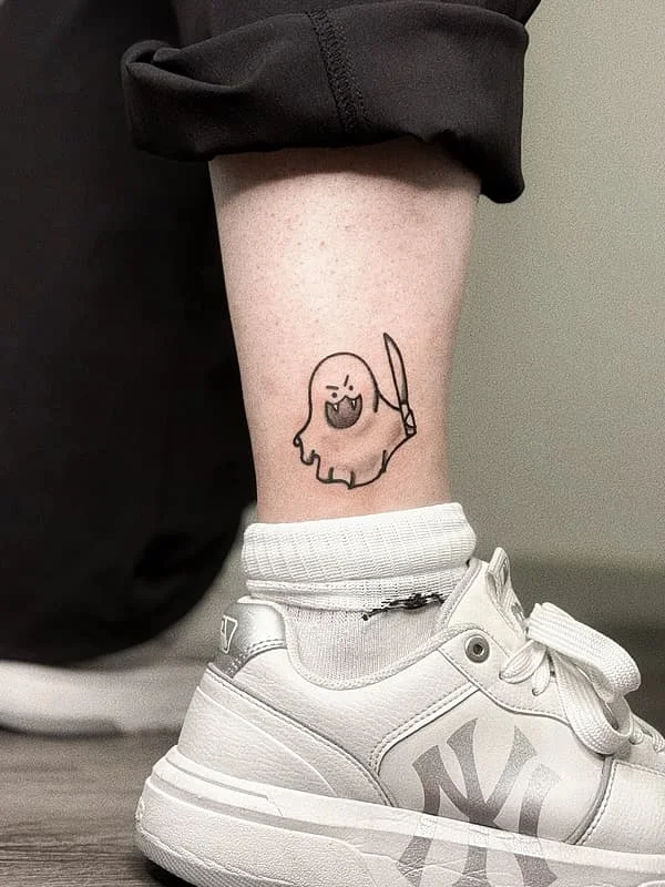 Cartoon ghost tattoo with a sword on ankle.